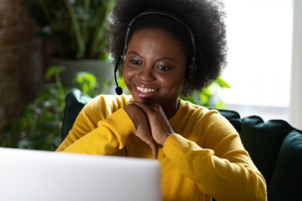 Smiling Afro woman wear headphones talk video calling, using laptop, watching webinar work from home